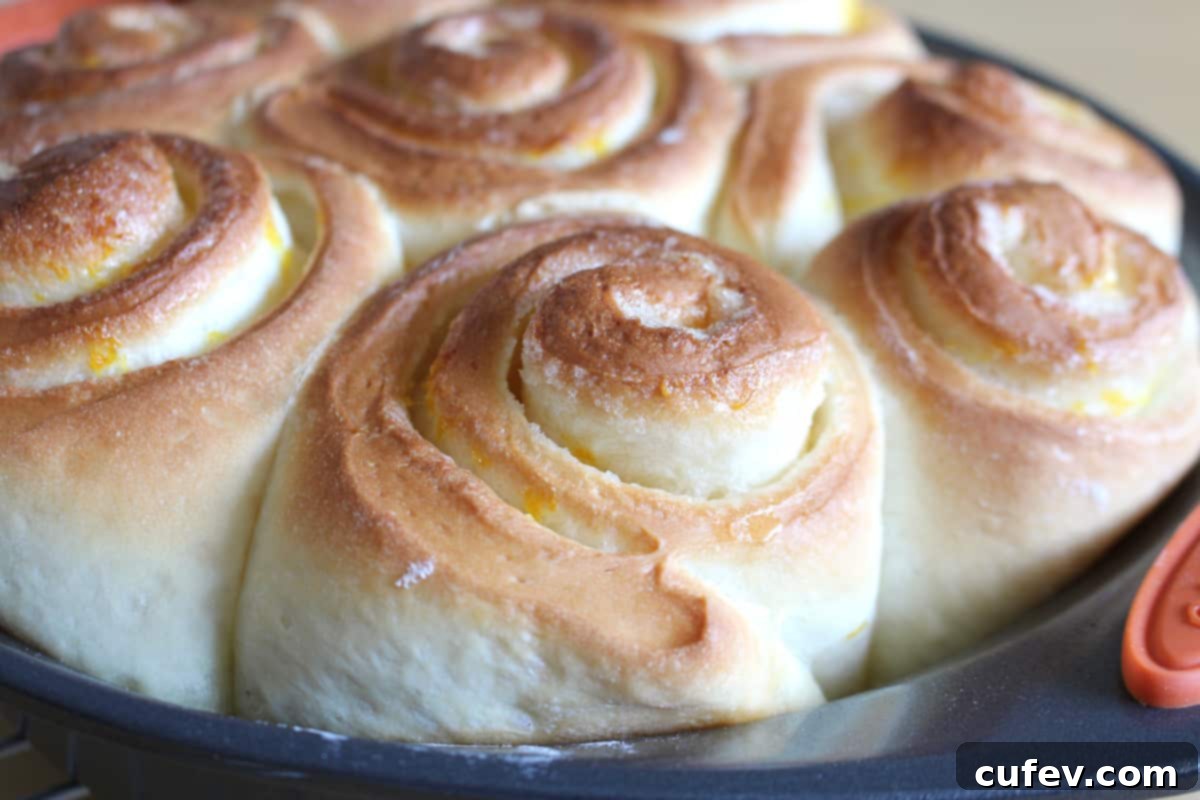 Freshly baked lemon cinnamon rolls, golden brown and glistening, cooling in a round pan straight out of the oven.