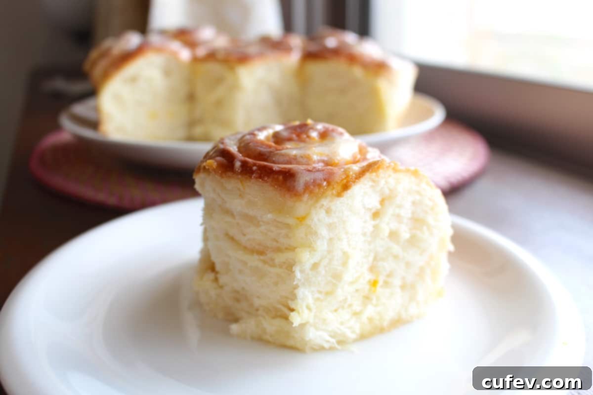 A straight-on close-up shot of a single fluffy lemon sweet roll on a plate, showcasing its soft texture and generous frosting.