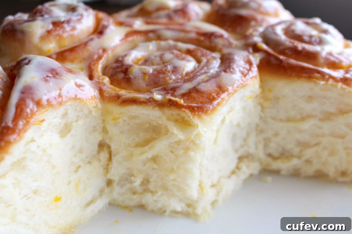 A close-up, 45-degree angle shot of several fluffy, iced lemon rolls nestled together in a dark round baking pan, ready to be served.