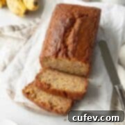 A sliced loaf of gluten free banana bread on sheets of parchment paper and a knife laying next to it.