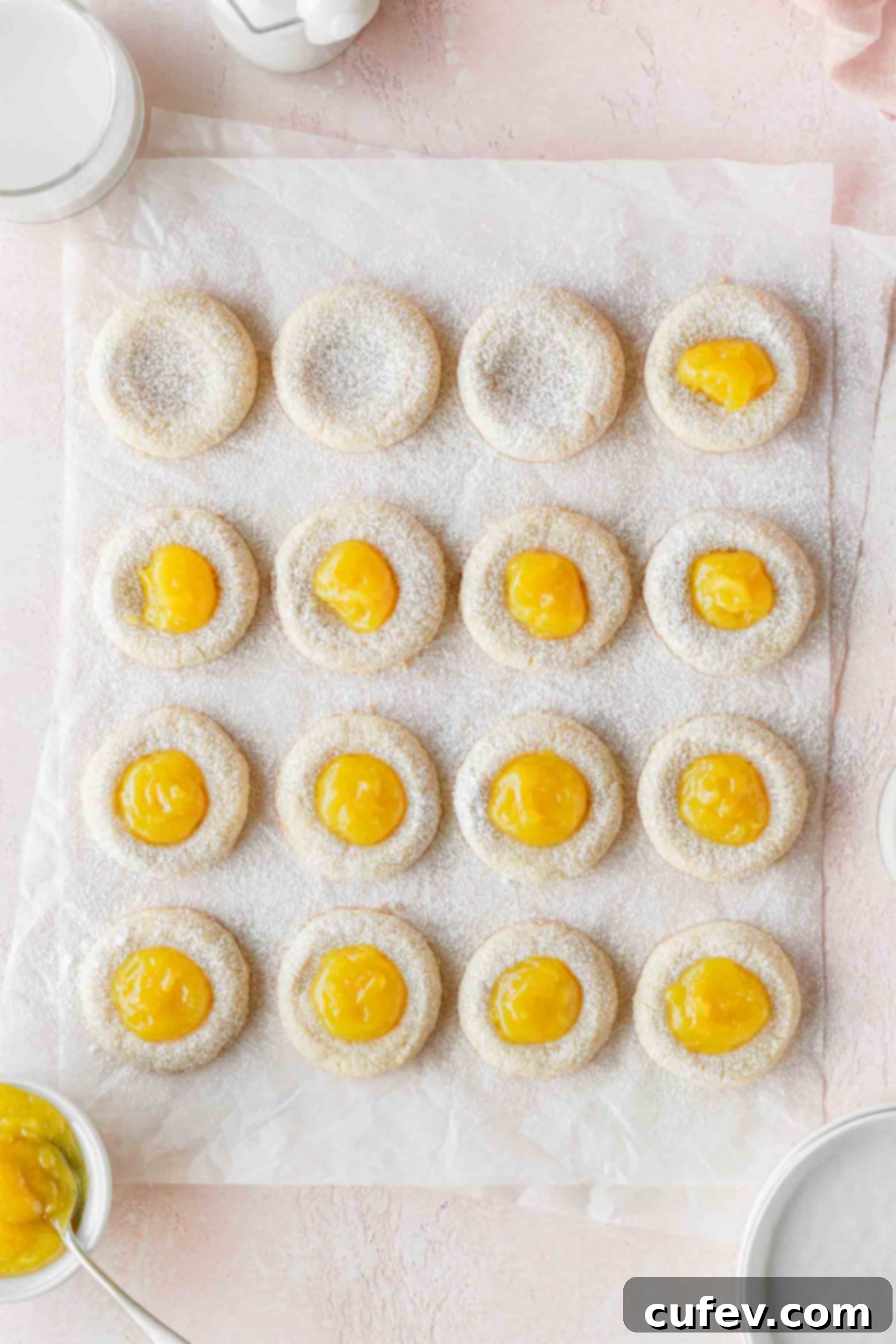 A close-up shot of lemon thumbprint cookies being meticulously filled with bright, homemade lemon curd.