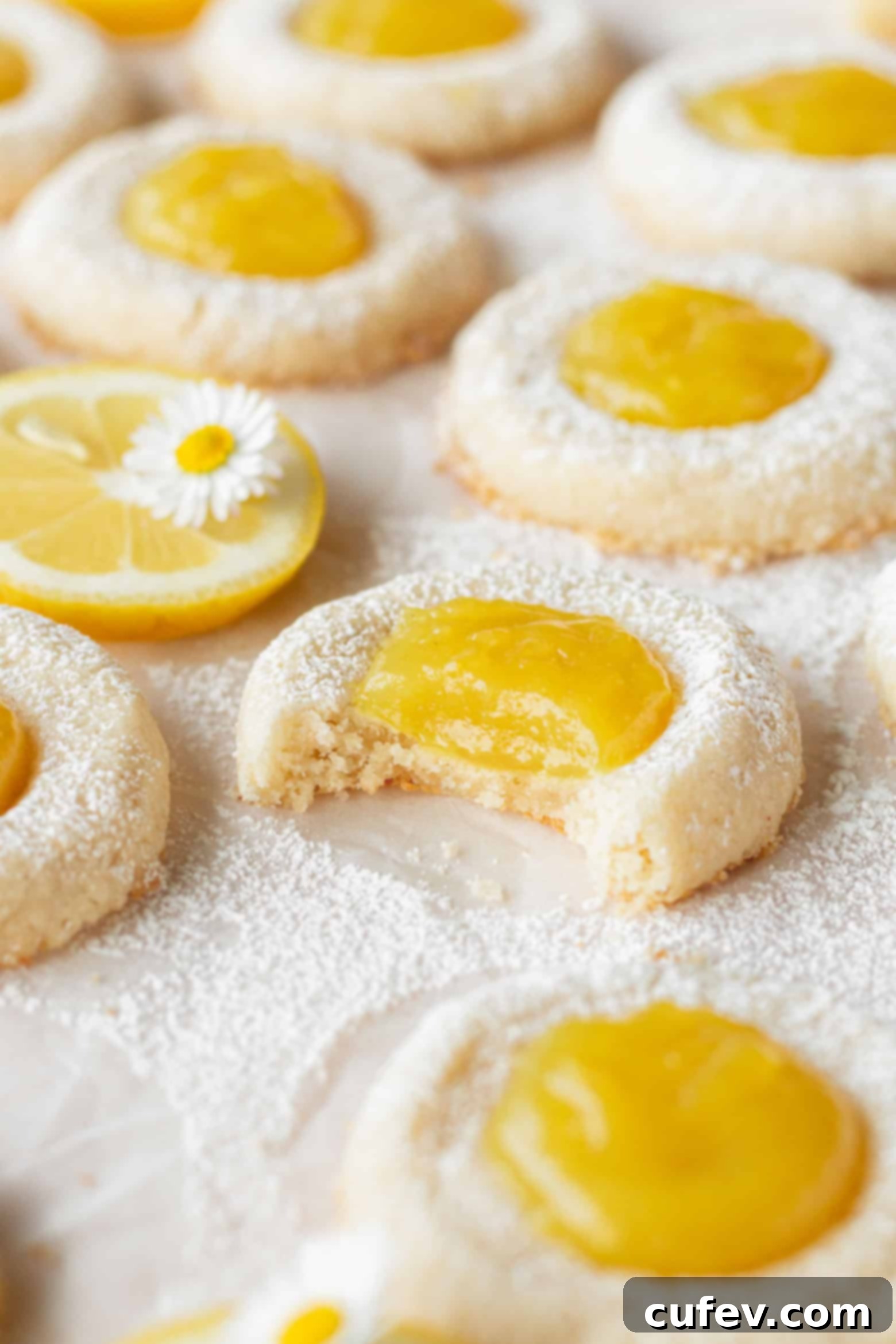 A perfectly bitten lemon thumbprint cookie, showcasing its tender base and tangy curd, surrounded by many other tempting cookies.