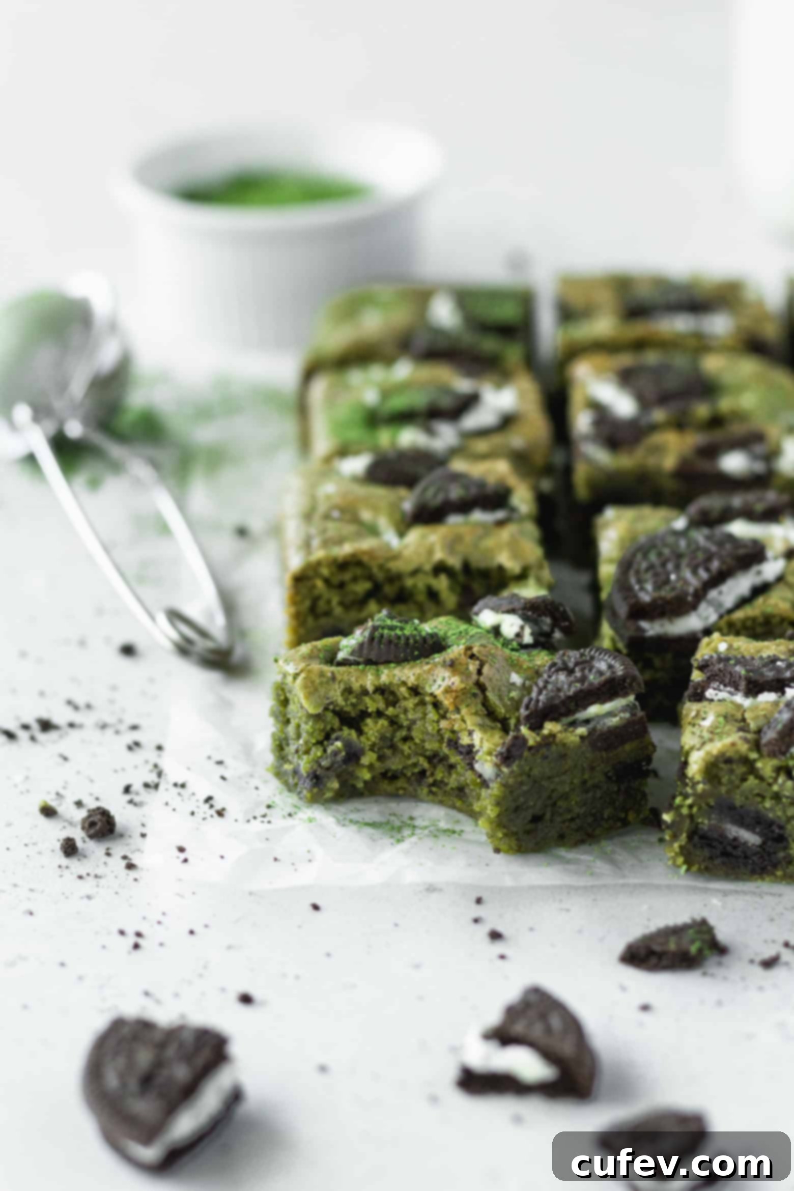 A close-up of a bitten square of matcha blondie, showing the internal texture, green color, and embedded Oreo pieces.