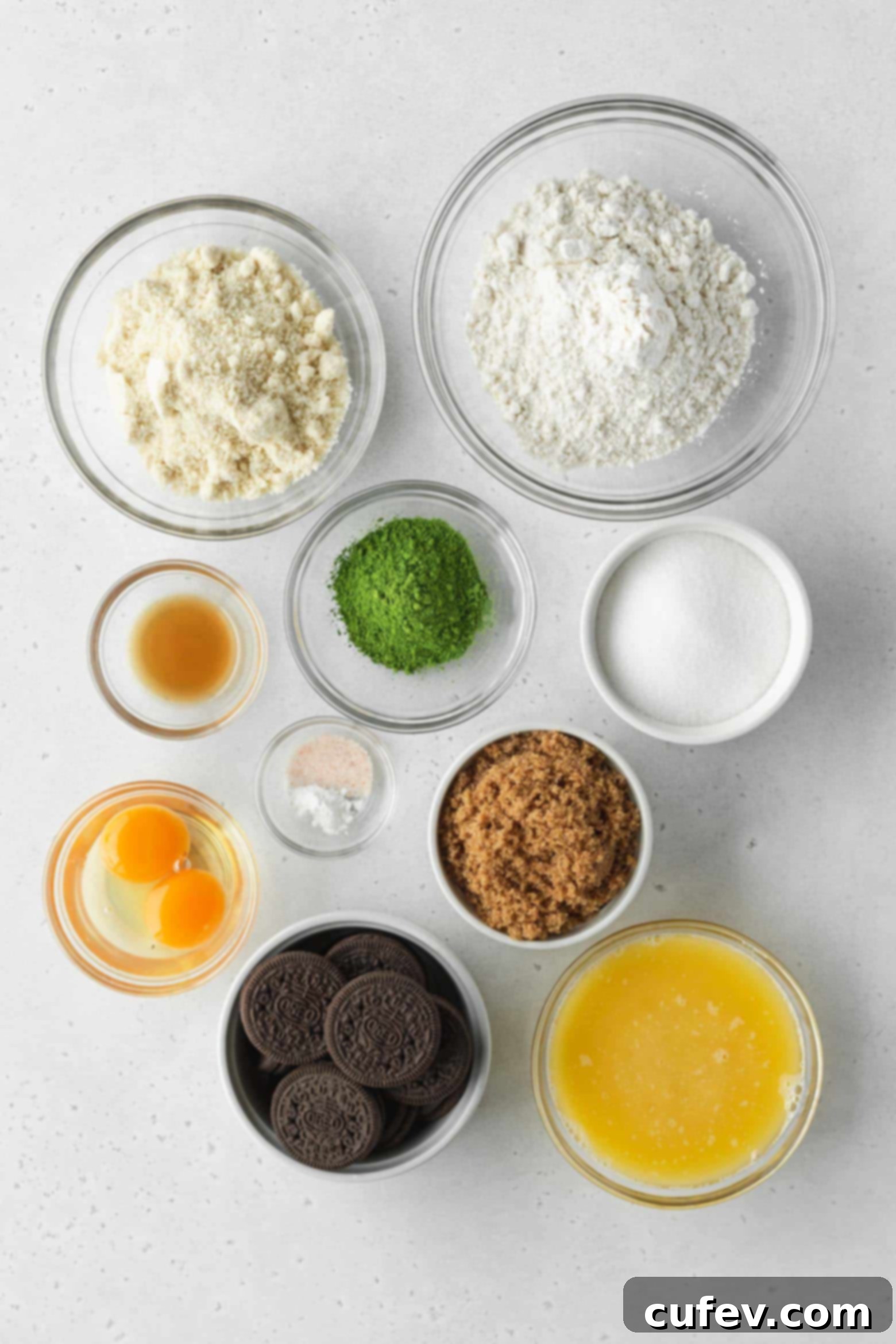 A selection of key ingredients laid out: flour, matcha powder, butter, brown sugar, eggs, vanilla, and crushed Oreos.