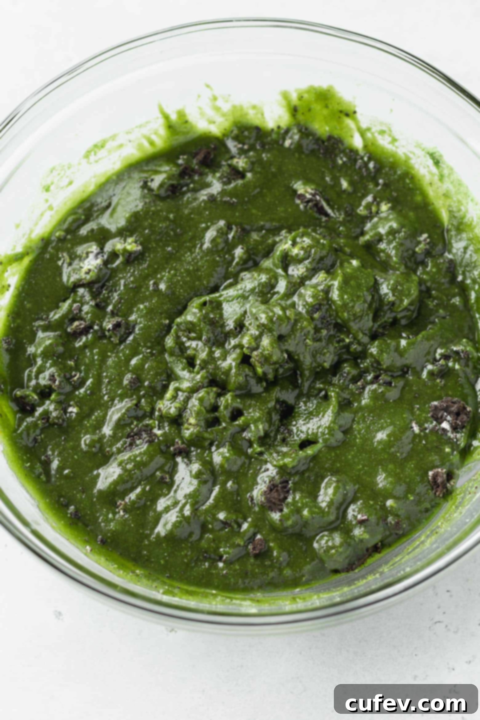 Vibrant green matcha blondie batter being mixed in a clear glass bowl.