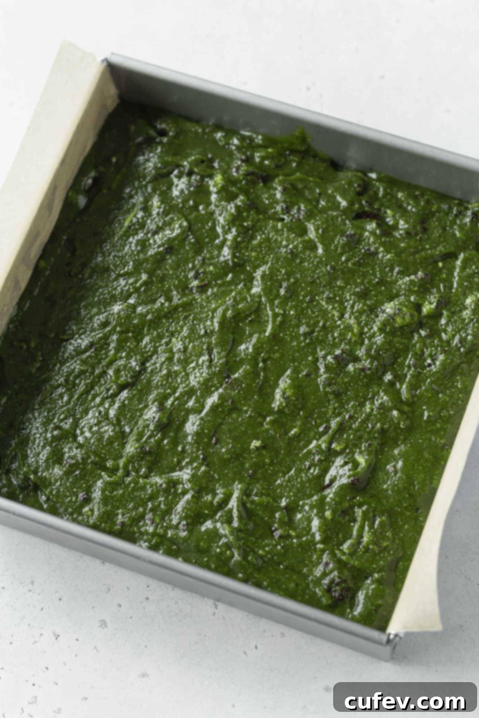 Matcha blondie batter spread evenly into a parchment-lined square baking pan, ready for the oven.