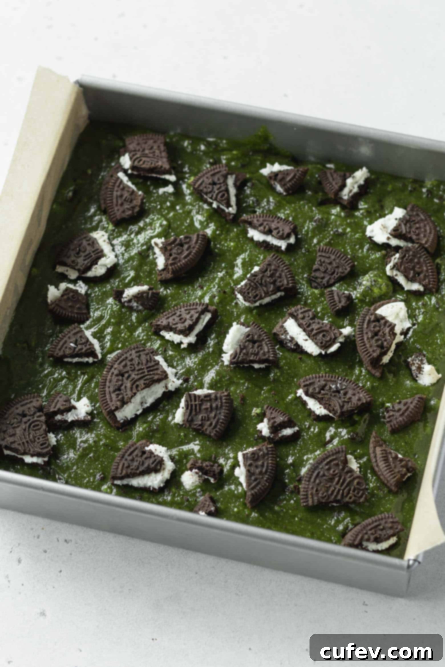 Close-up of crushed Oreo pieces sprinkled over the green matcha blondie batter in the baking pan.