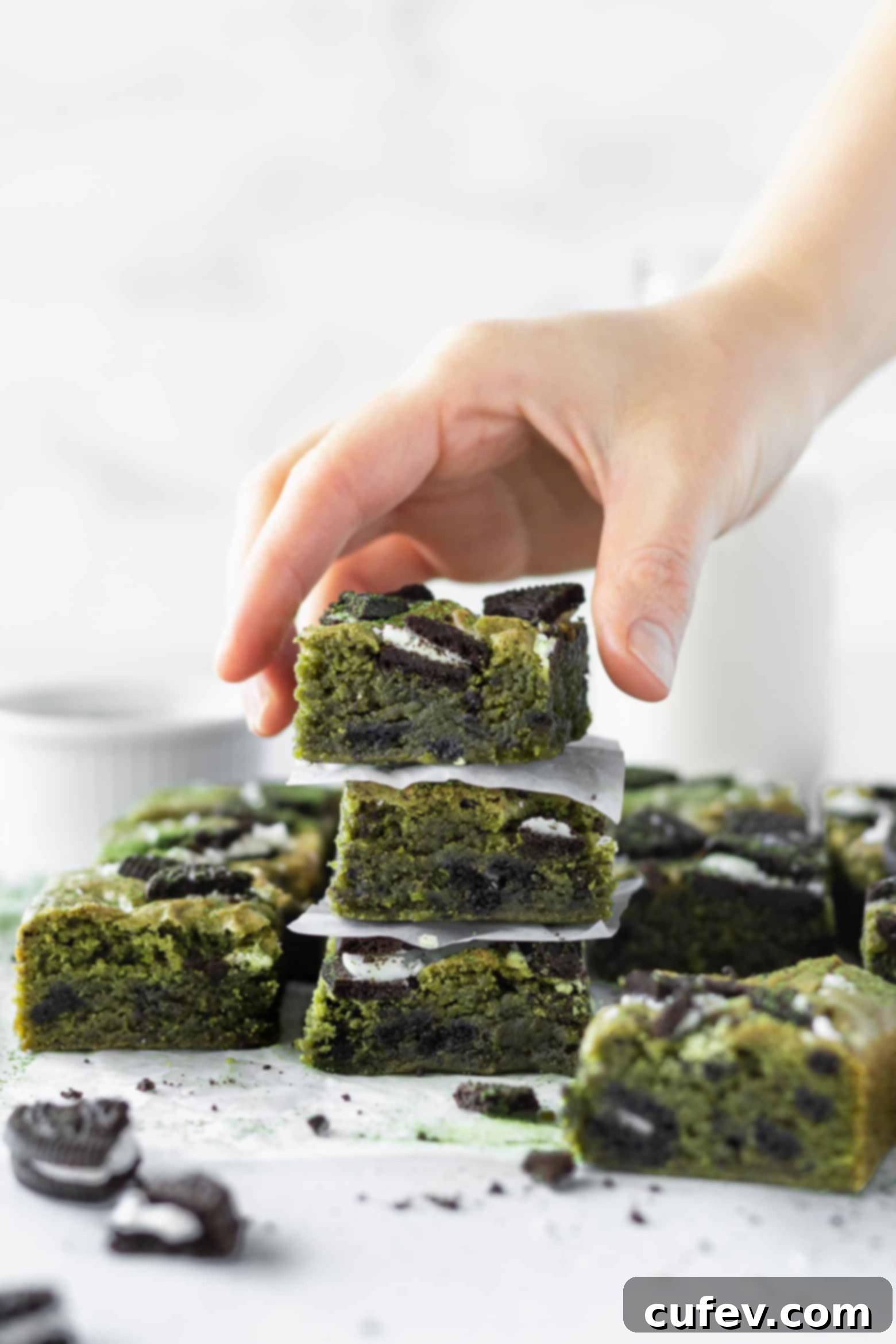 A hand reaching for a stack of three vibrant green matcha Oreo blondie squares, showing off their generous size.