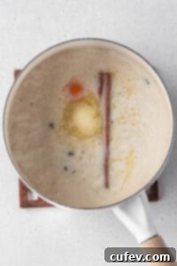 A pot of partially cooked rice infused with evaporated oat milk, vegan butter, cinnamon stick, and orange peel, ready to simmer.