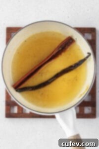 A small pot containing sugar, water, agave, a cinnamon stick, and a vanilla bean pod simmering to create a fragrant syrup.