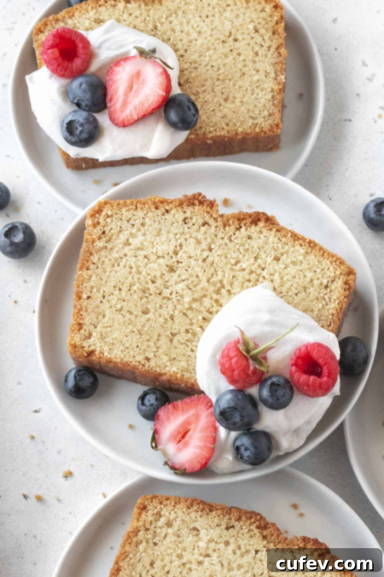 A beautifully sliced gluten-free pound cake on a white plate, garnished with whipped cream and fresh mixed berries.