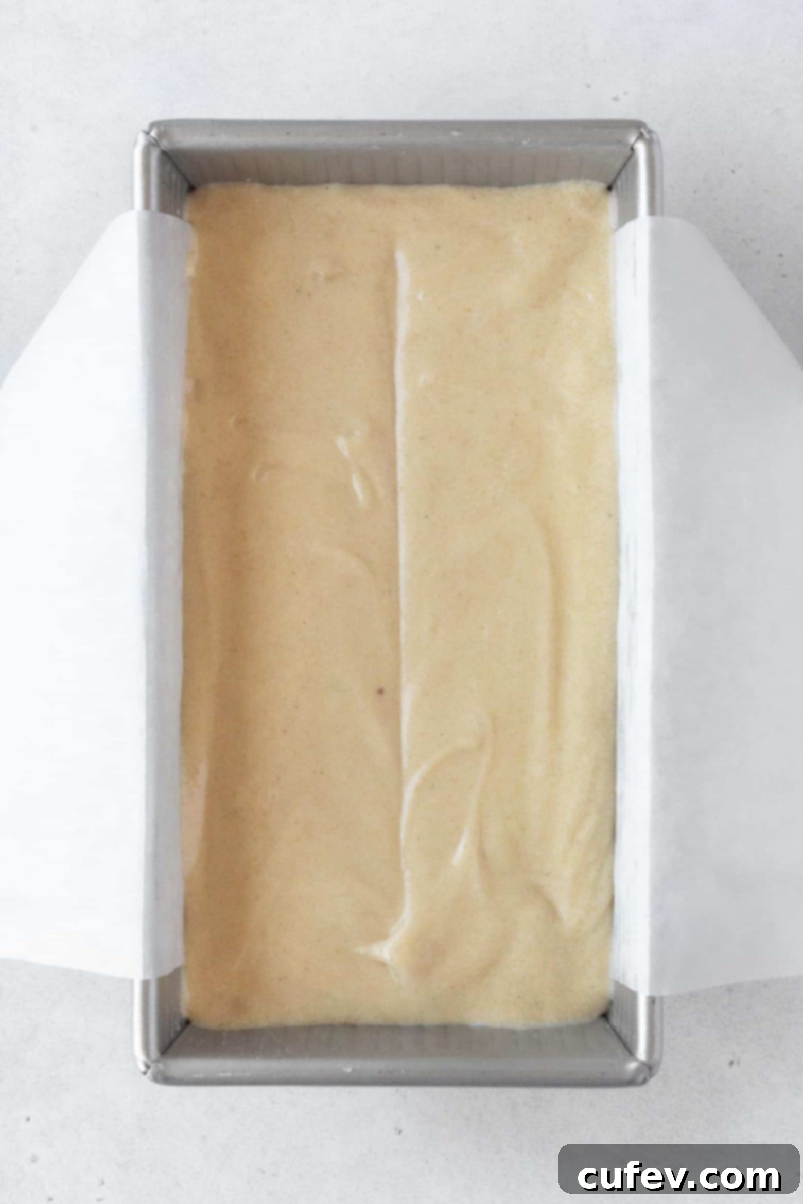 Pouring the smooth gluten-free cake batter into a parchment paper-lined loaf pan.