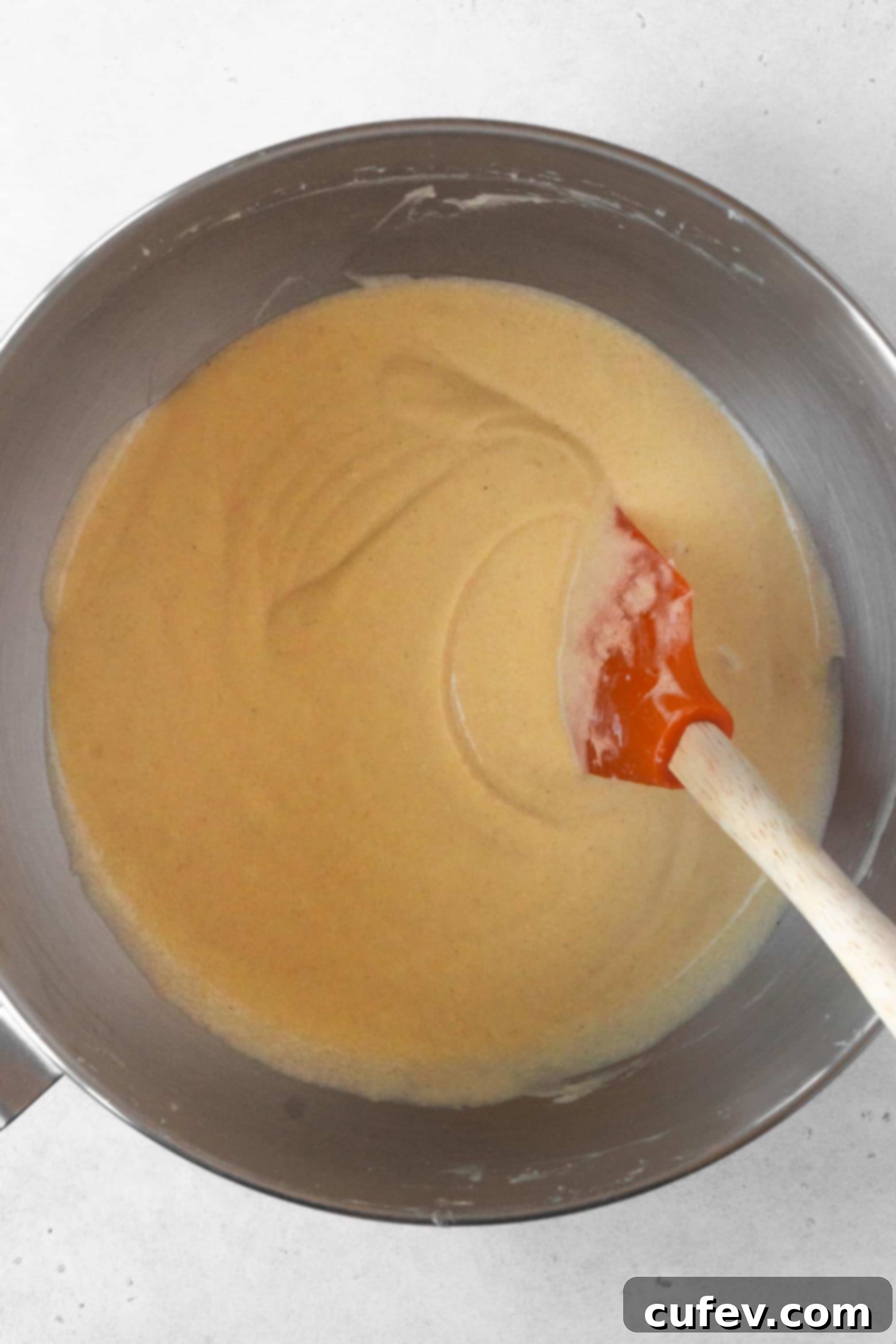 Scraping down the sides of the mixing bowl to ensure the pound cake batter is thoroughly combined and homogenous.