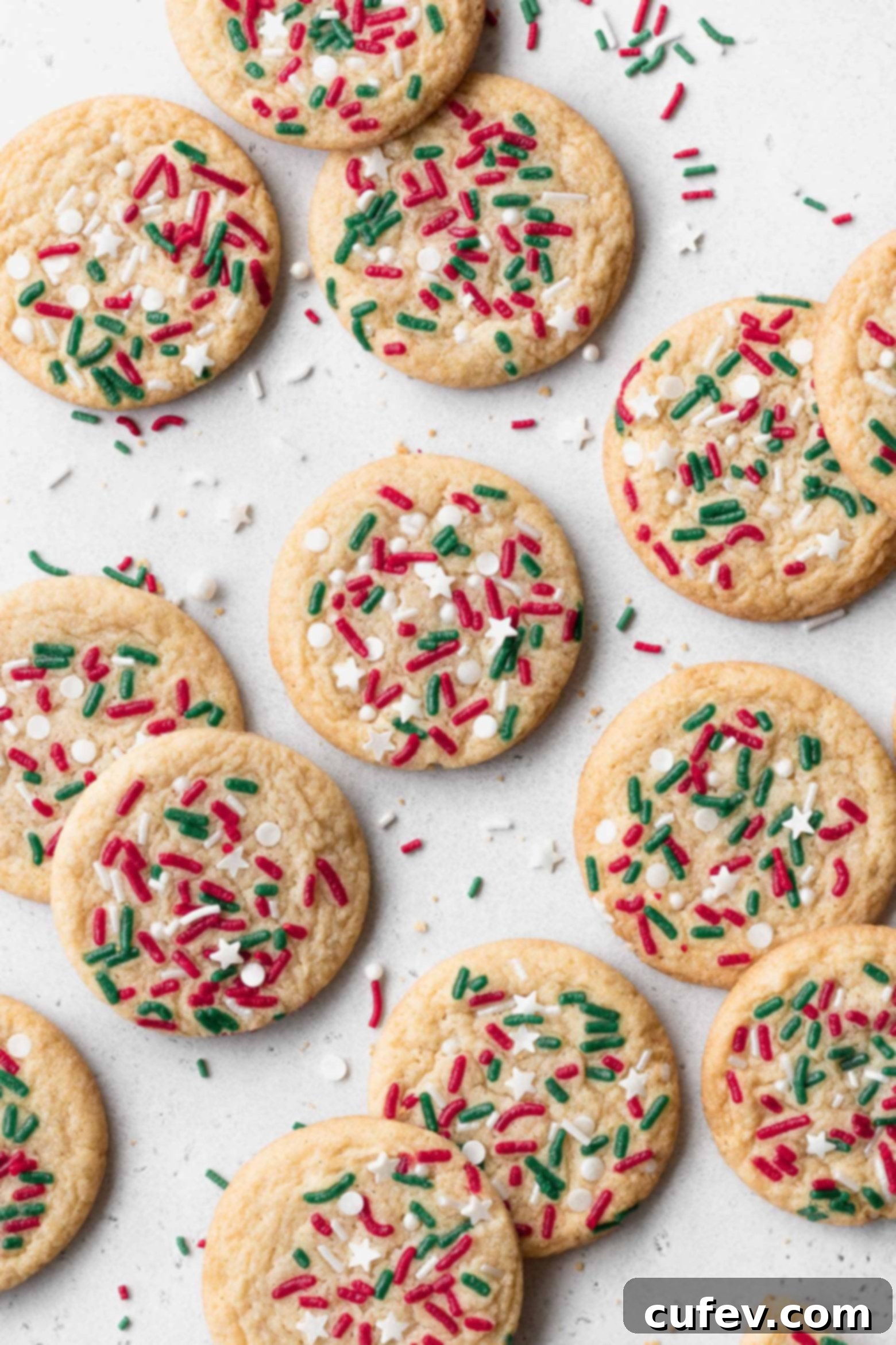 Christmas sugar cookies with sprinkles on a white surface.