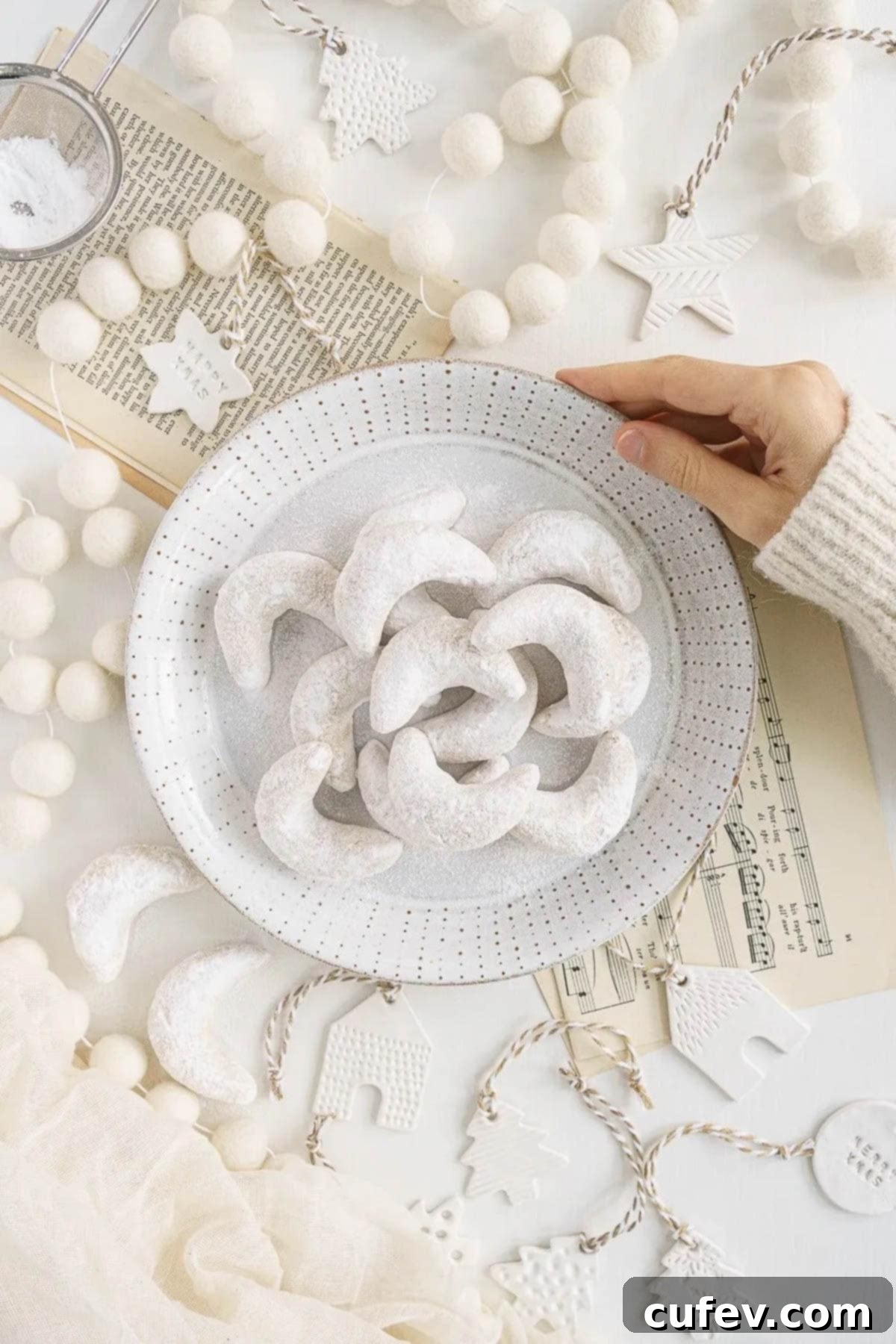 A hand holding a plate of almond crescent cookies covered in powdered sugar.