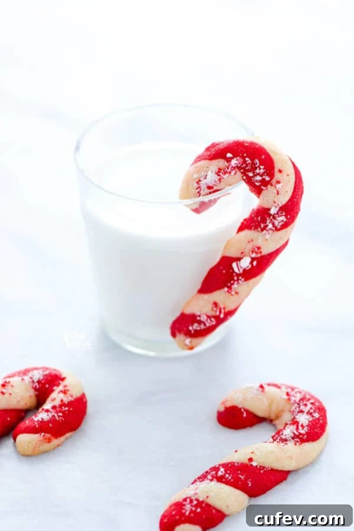 A candy cane shaped cookie hung on a glass of milk.