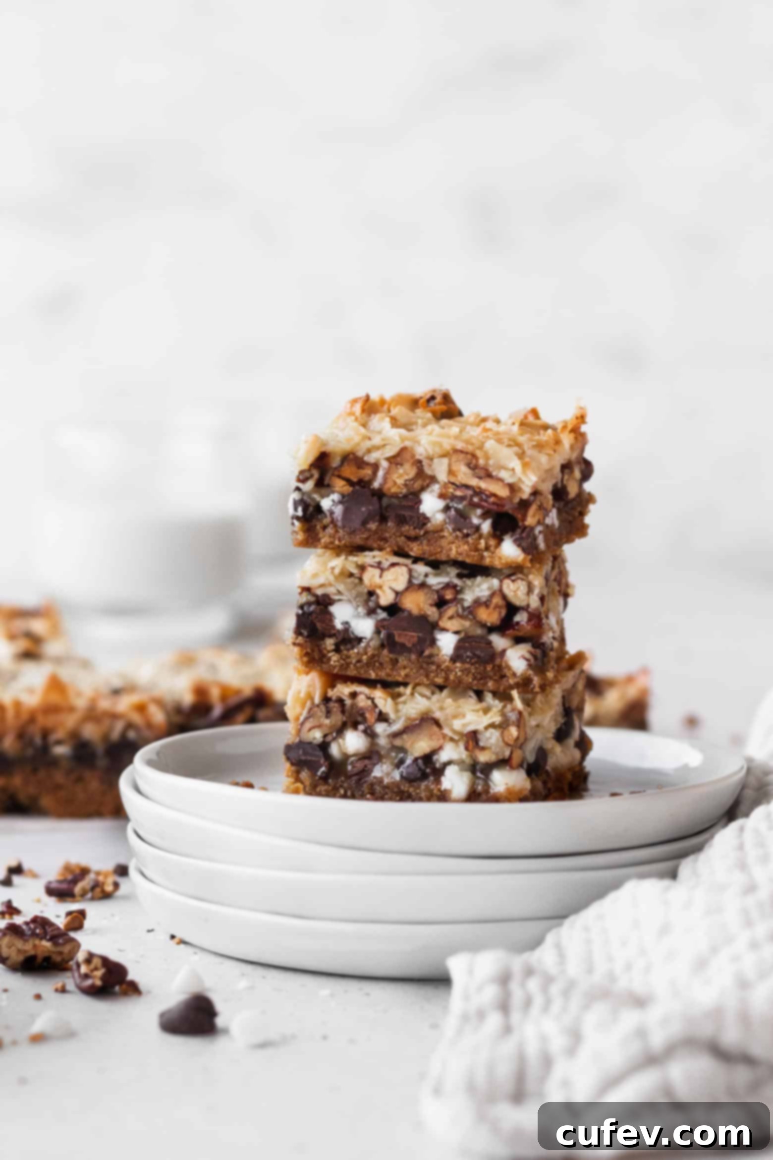 A stack of golden brown vegan magic bars on white plates, showcasing their distinct layers.