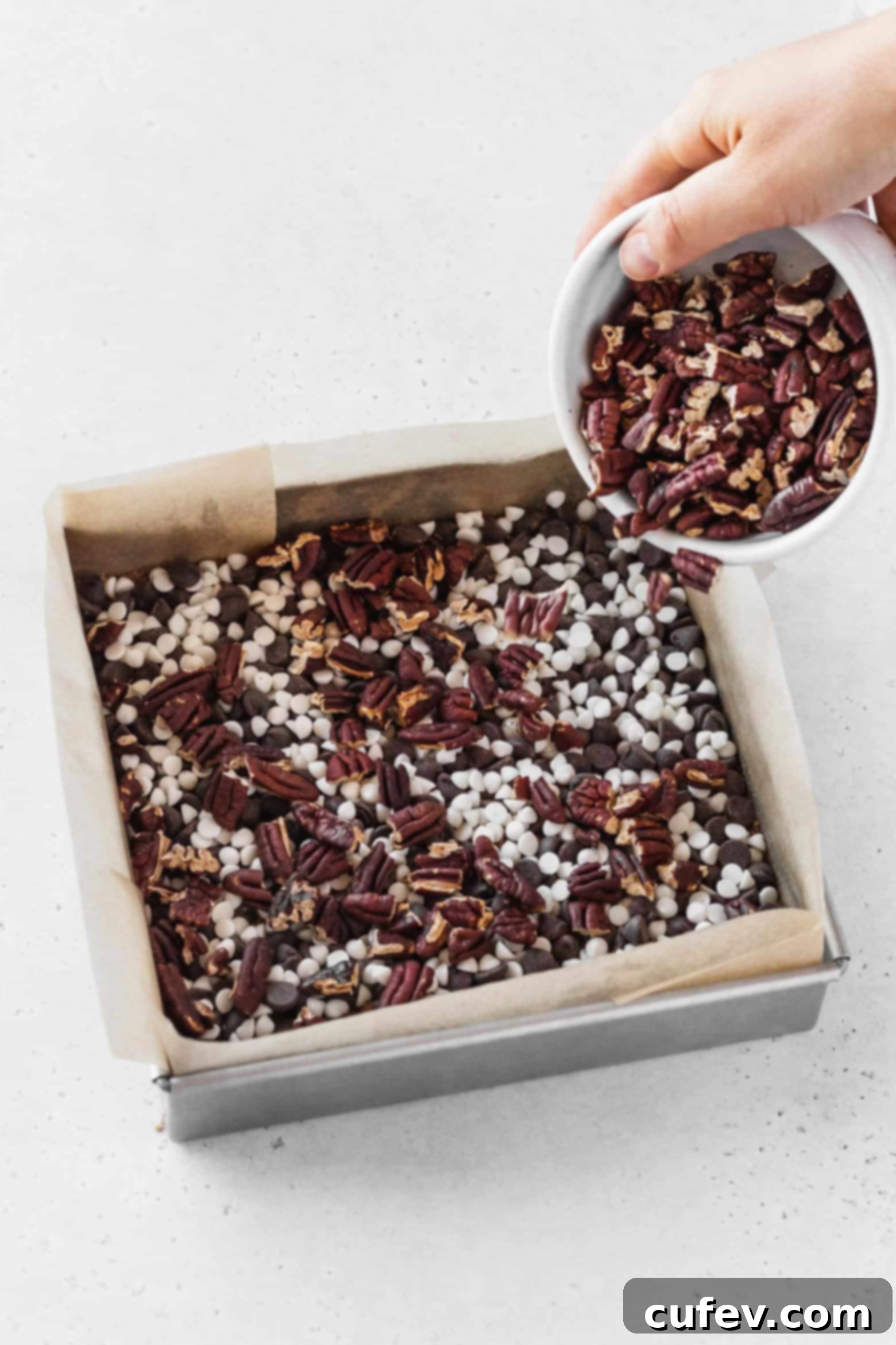 Adding a layer of chopped pecans carefully over the chocolate chips.