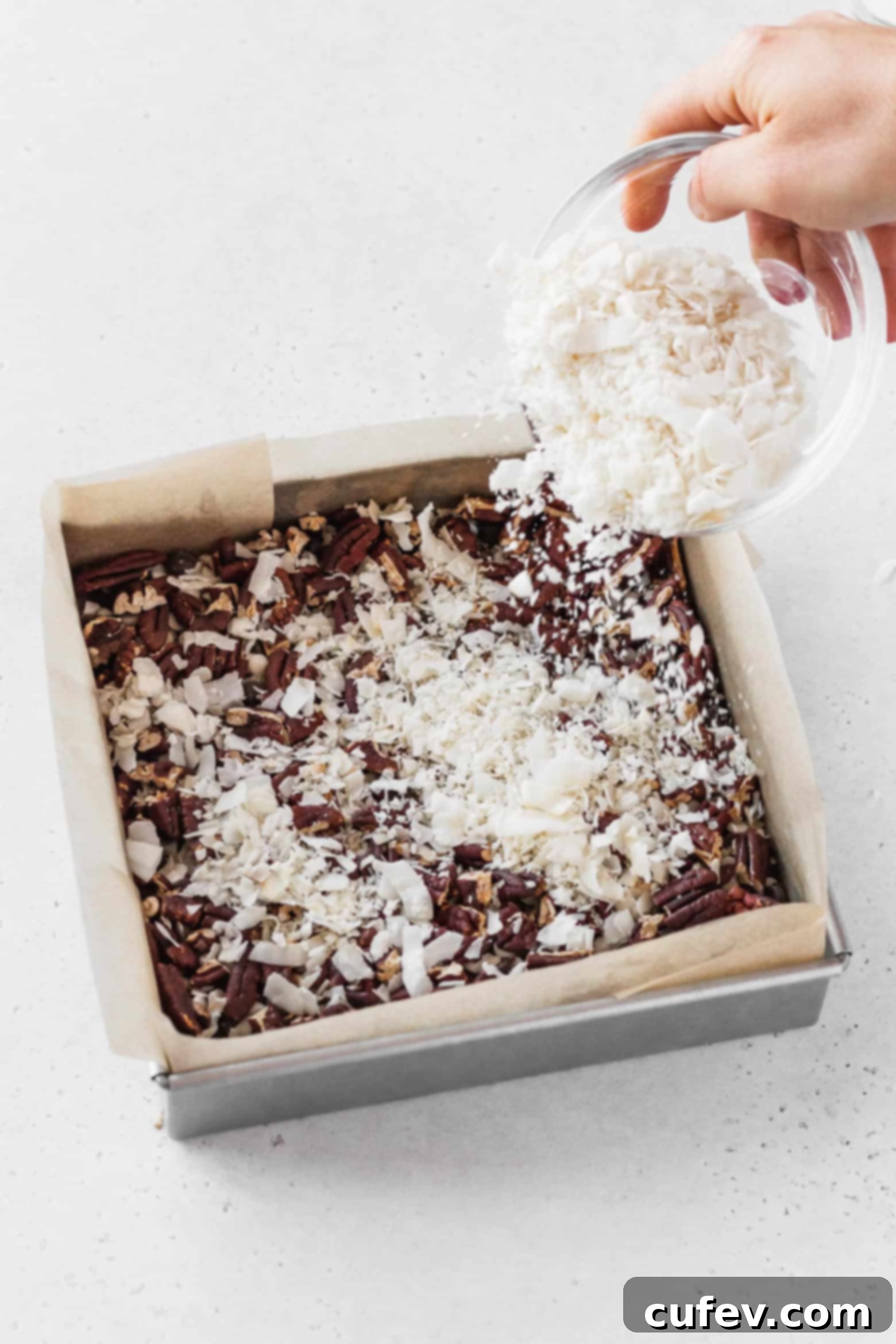 Sprinkling flaked coconut evenly over the chopped pecans.