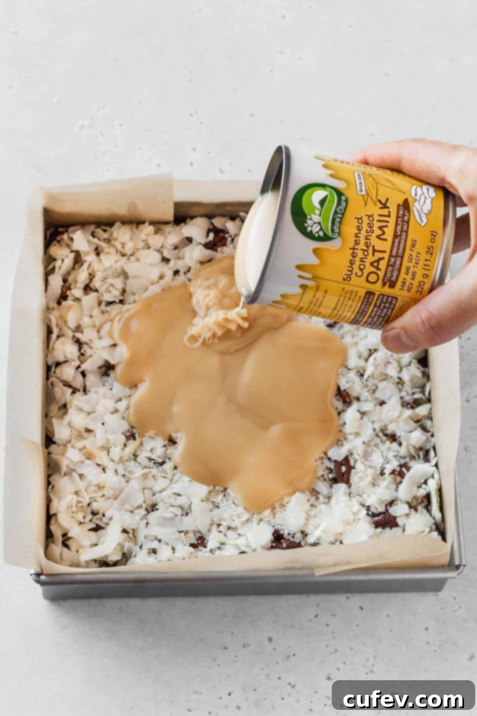 Pouring a can of vegan sweetened condensed milk over the coconut layer, ensuring even coverage.