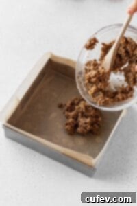 Putting the graham cracker mixture into a square pan.