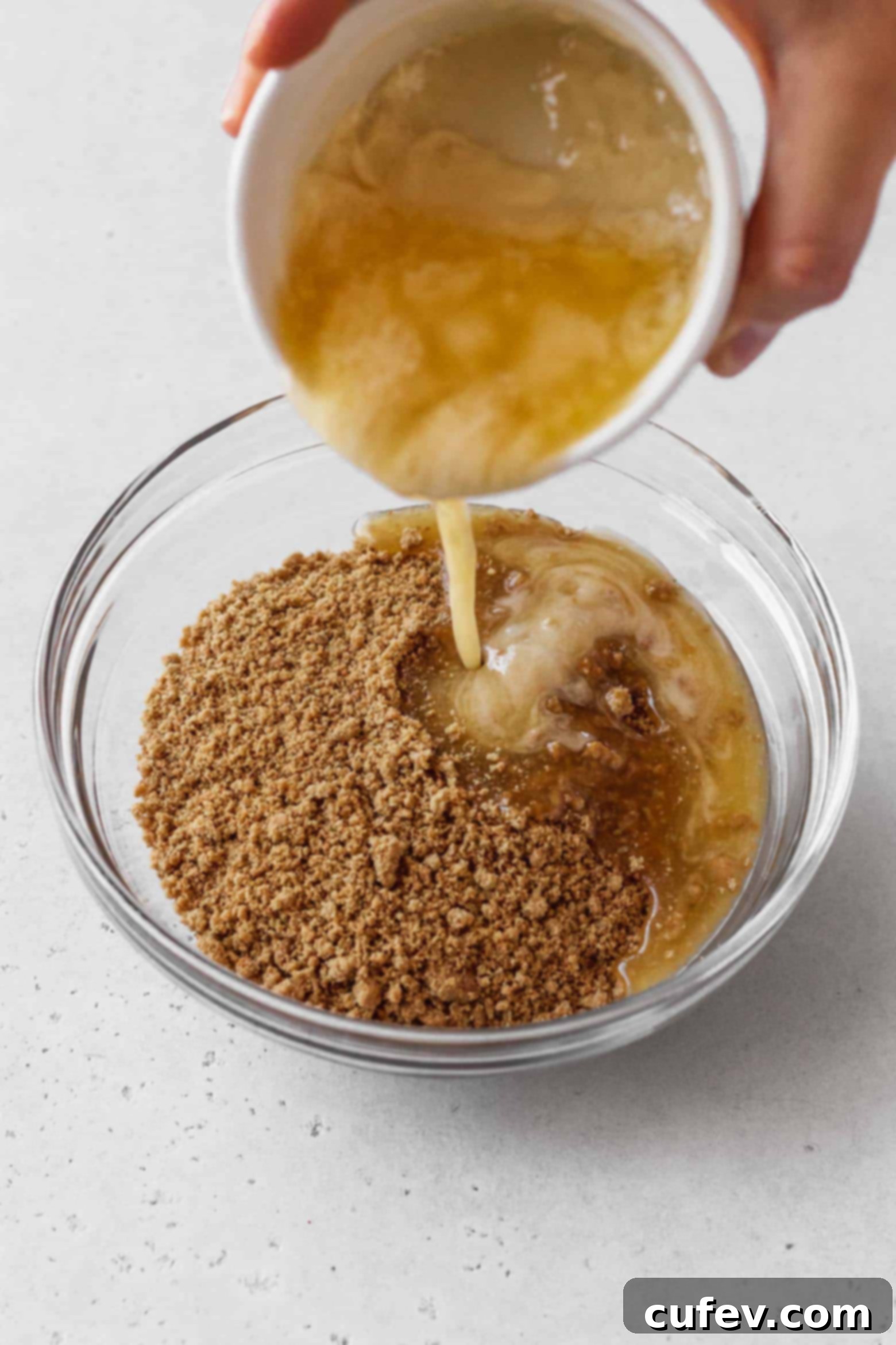 Melted vegan butter being poured into a bowl of graham cracker crumbs.