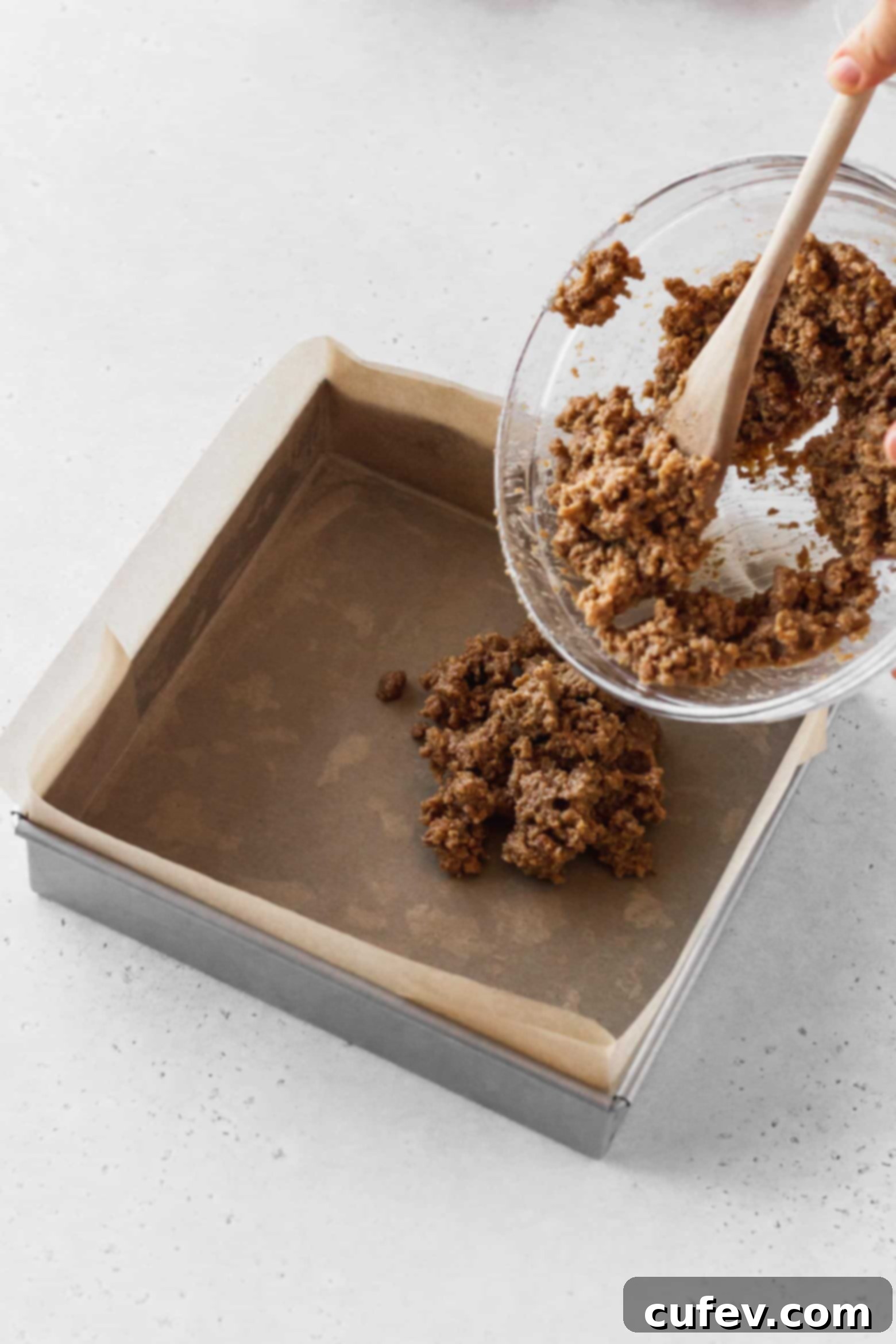 Pressing the graham cracker mixture into a square pan to form an even crust.