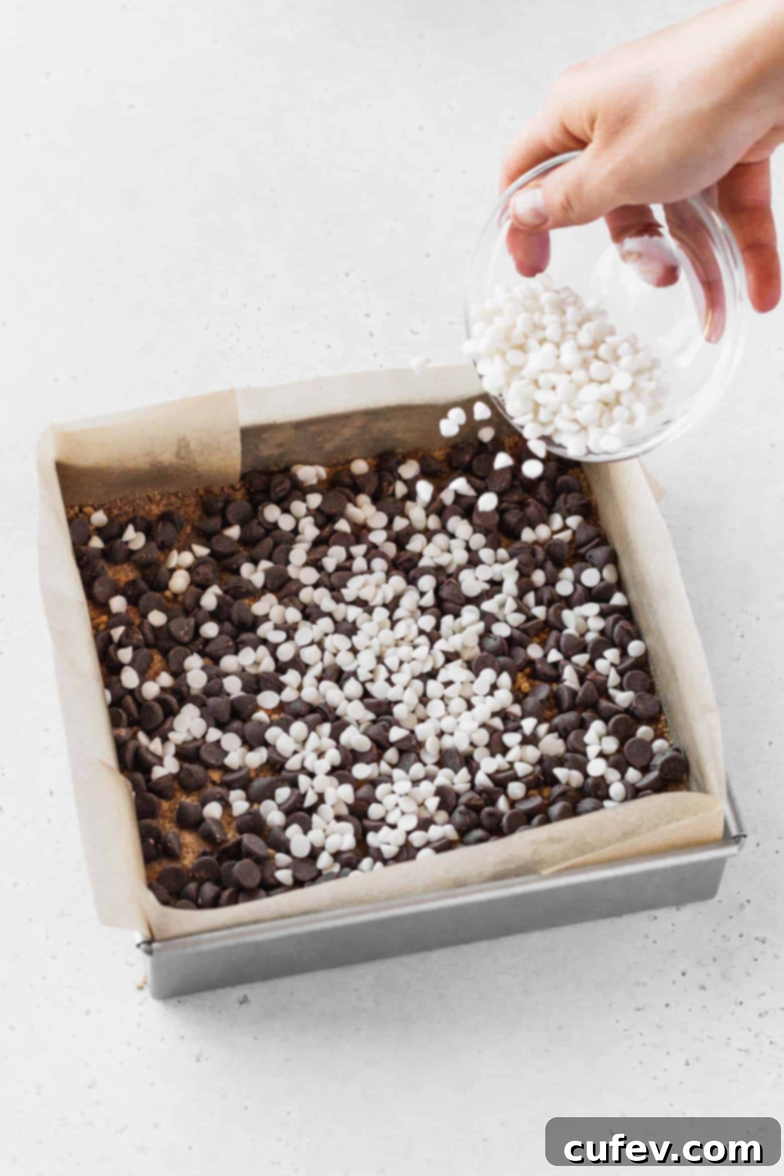 Adding a layer of vegan chocolate chips evenly over the graham cracker crust.