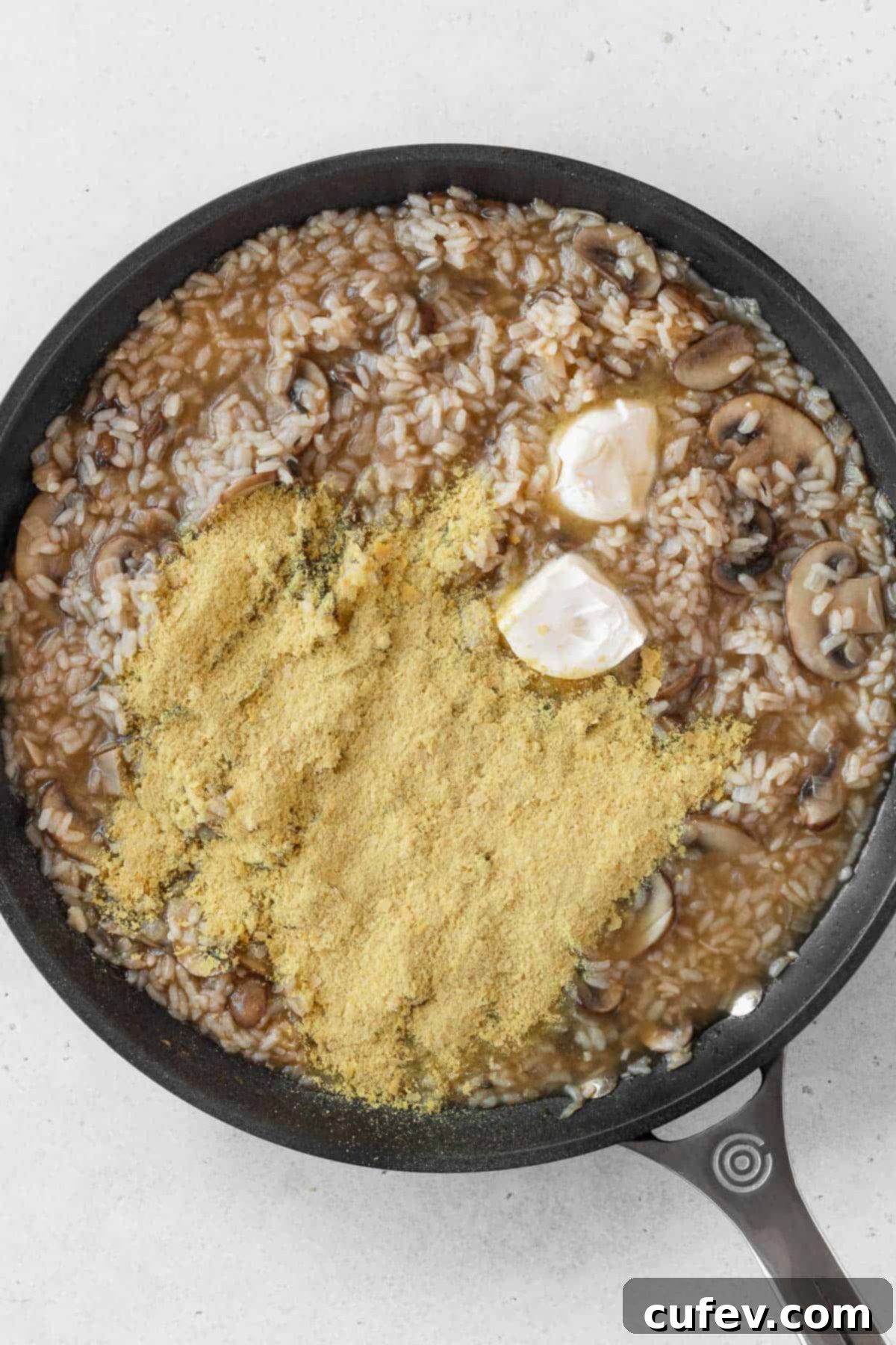 Vegan butter and nutritional yeast placed on top of hot mushroom risotto in a pan, about to be stirred in for creaminess.