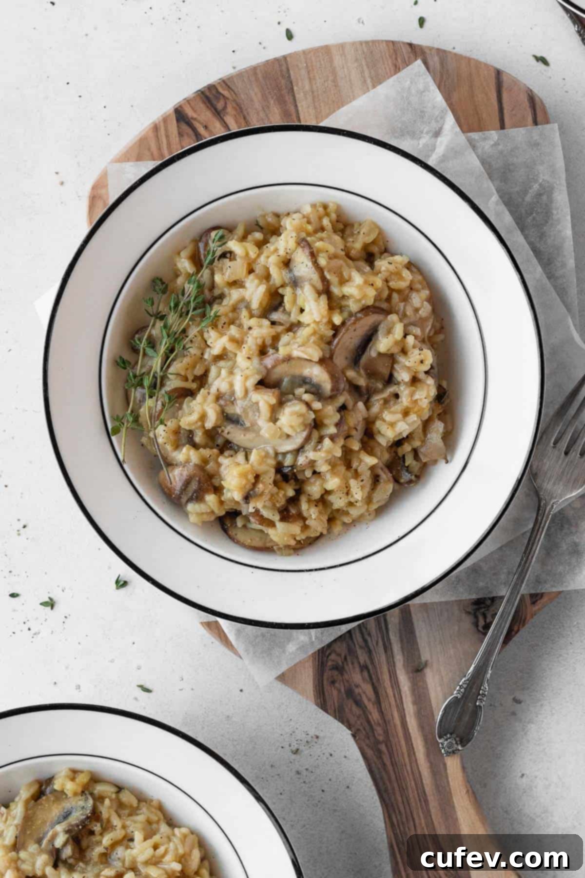 A pristine white bowl filled with creamy vegan mushroom risotto, garnished with a sprig of fresh thyme.