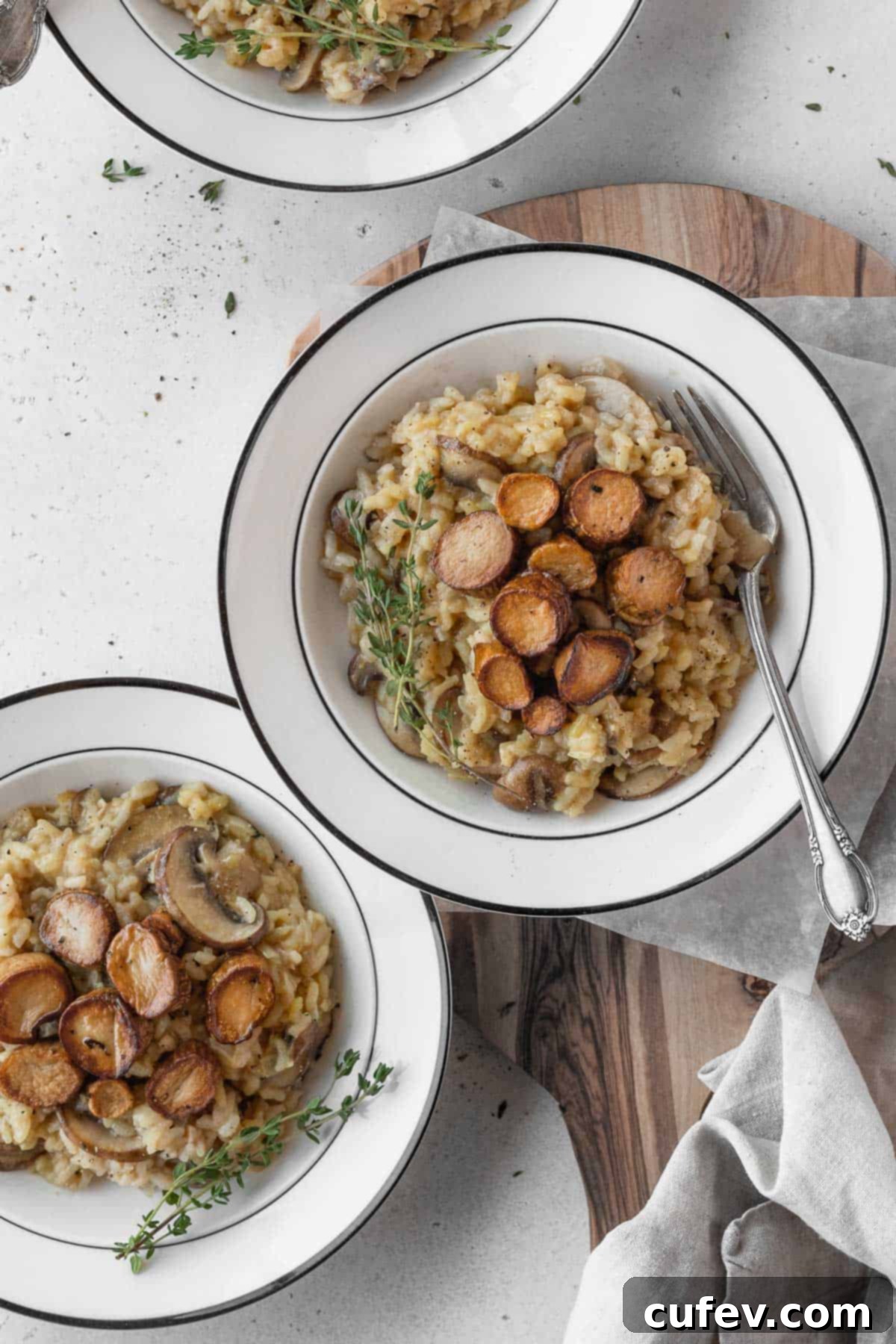 Two white bowls filled with creamy vegetarian risotto, garnished with fresh herbs and sliced mushrooms.
