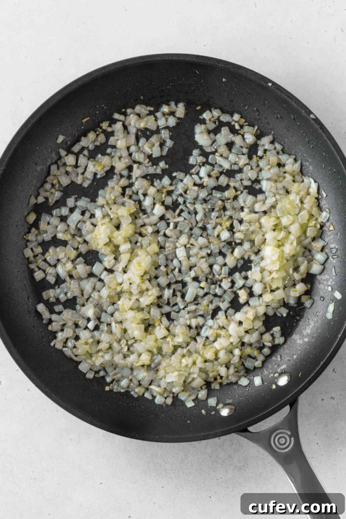 Close-up shot of finely chopped onions and minced garlic sautéing in olive oil in a pan, turning translucent.