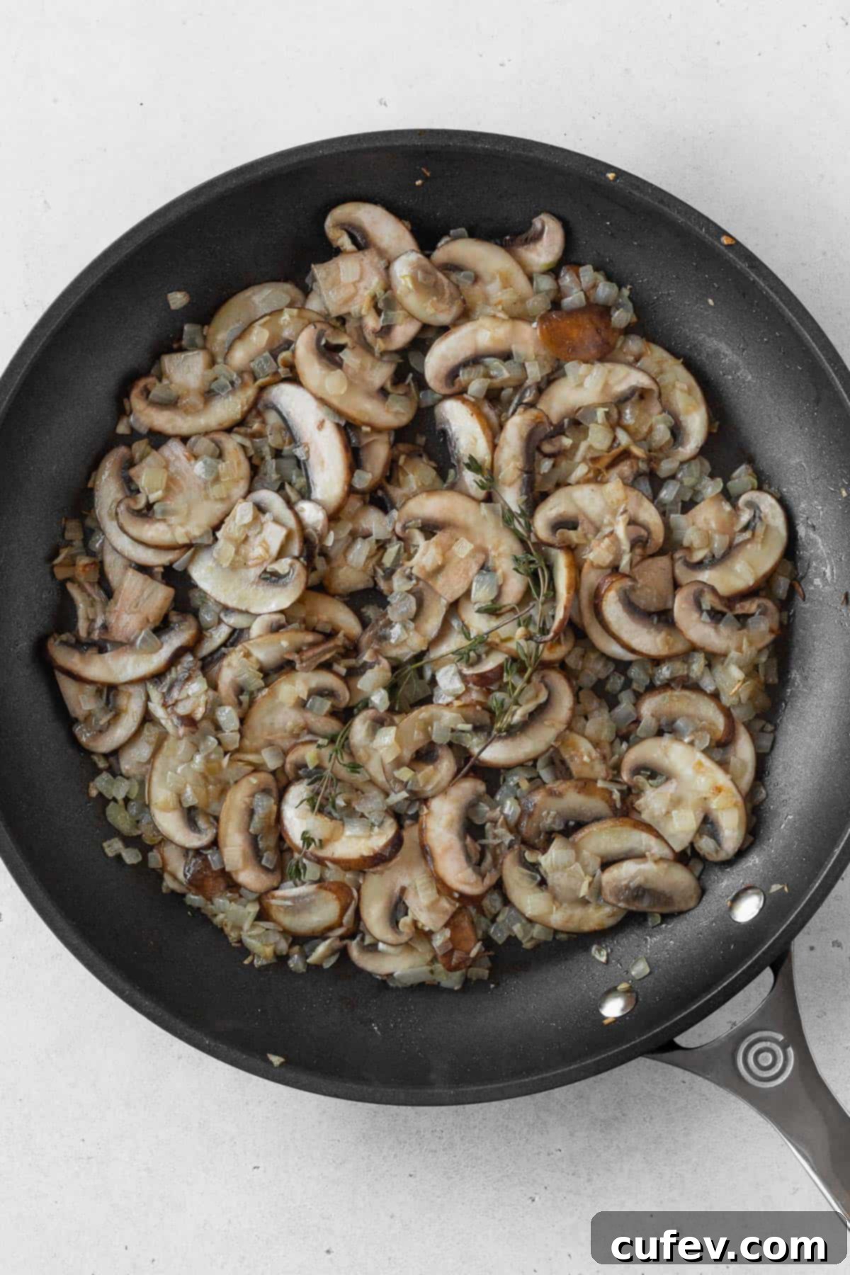 Sliced cremini mushrooms being added to the sautéed onions and garlic in a pan, ready to cook down.