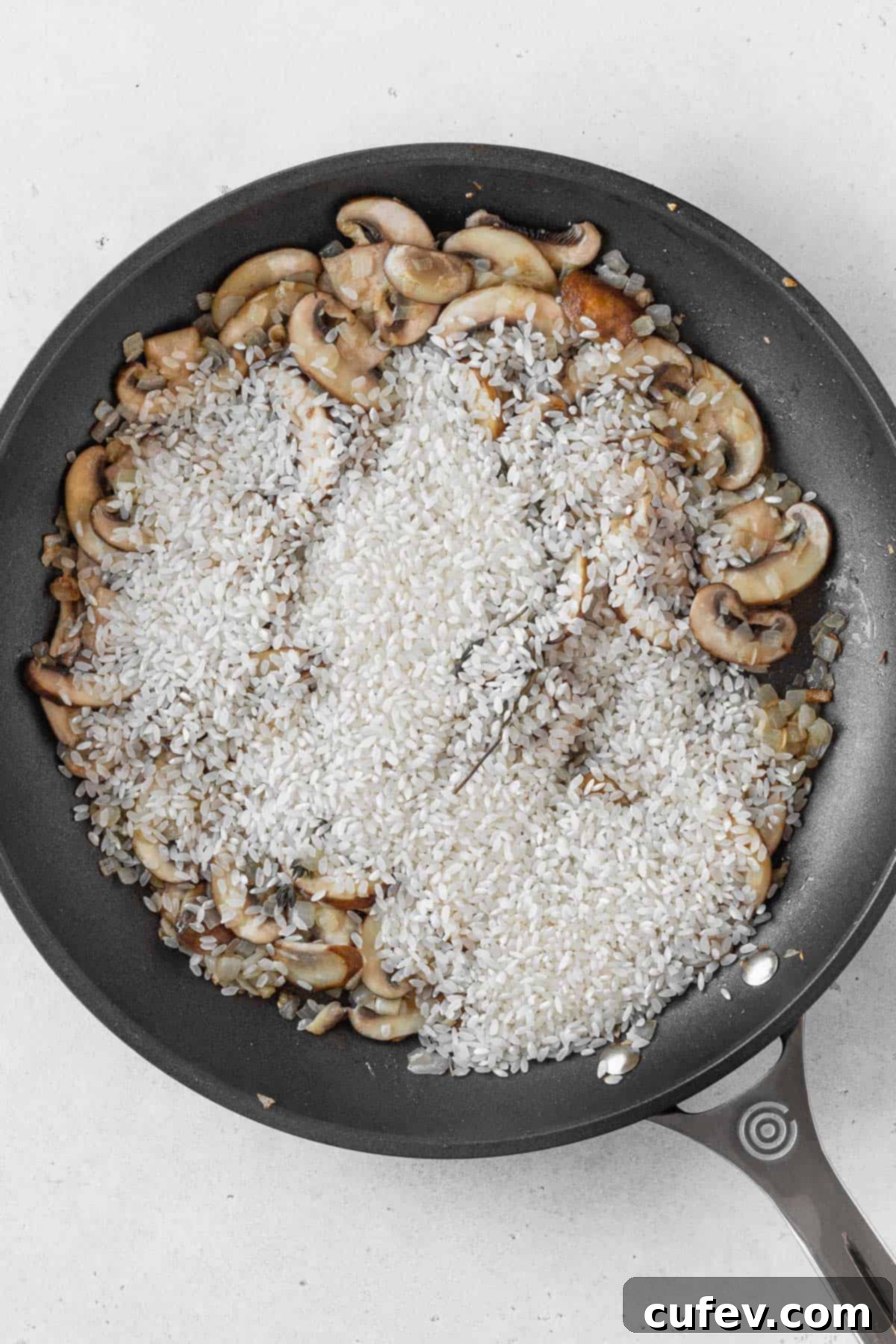 Arborio risotto rice being added to the pan with sautéed onions, garlic, and mushrooms, ready for toasting.