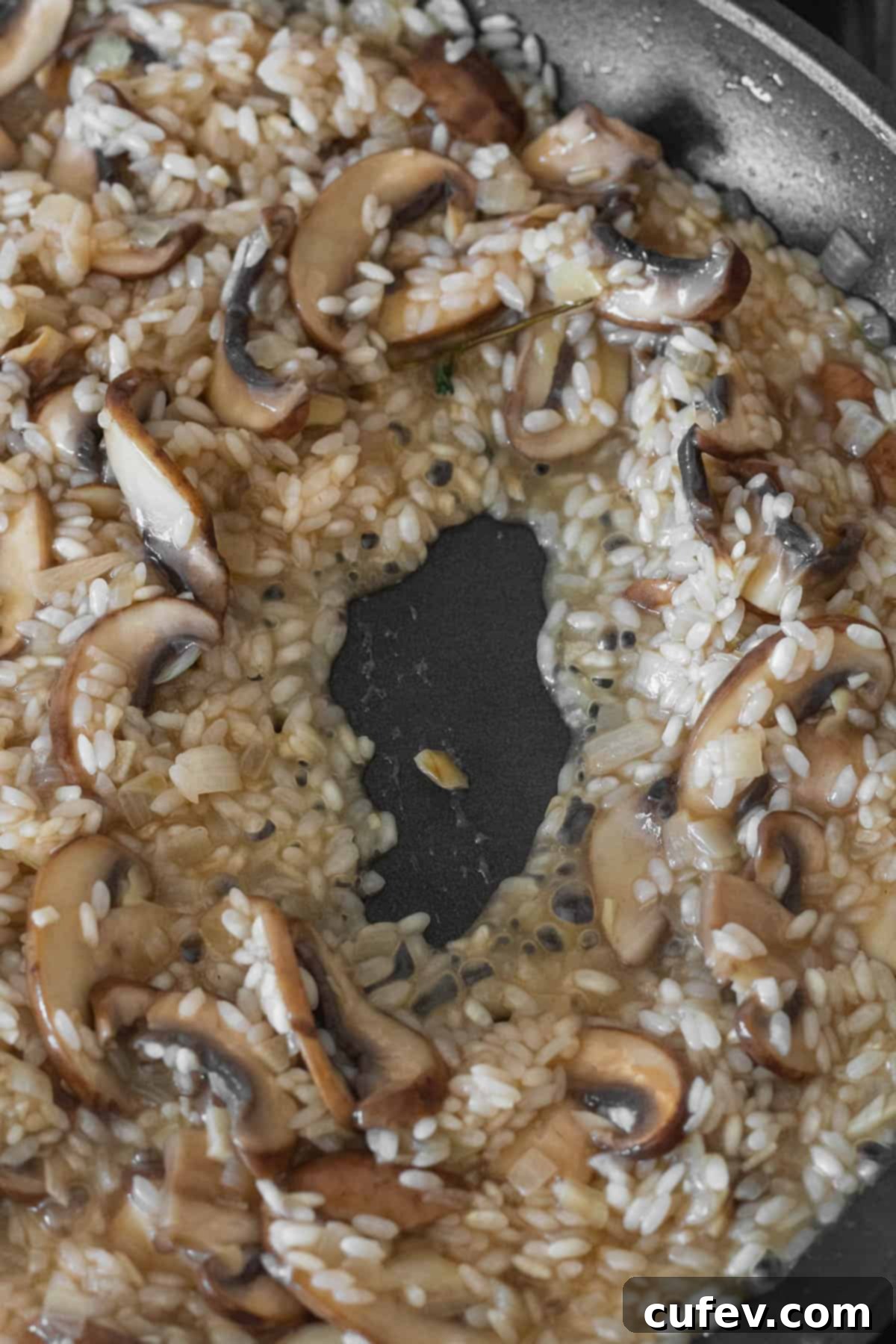 Close-up of risotto rice simmering and absorbing the vegetable stock in a pan, gradually becoming creamy.