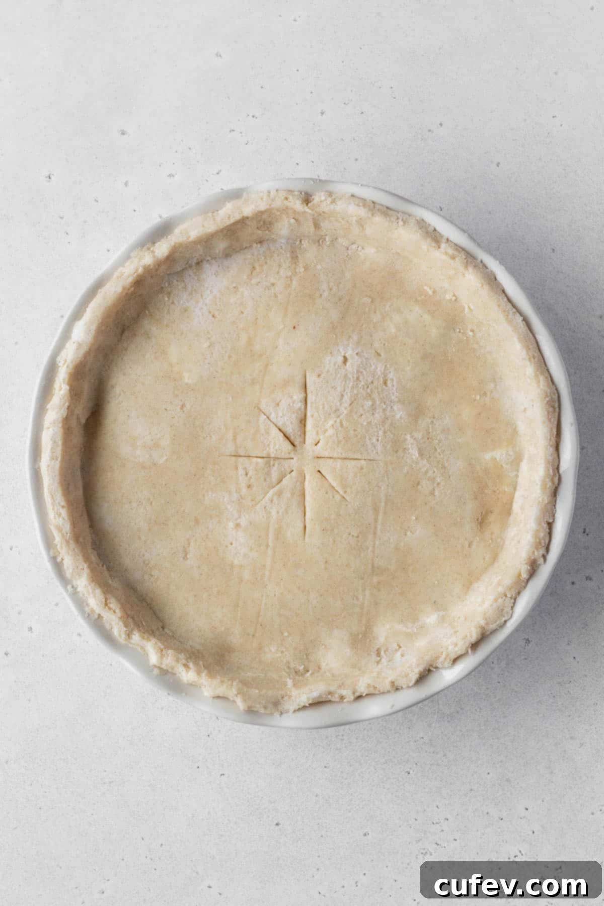 A pristine, unbaked vegan pot pie, elegantly topped with its golden crust and vent slits, resting on a neutral grey surface, anticipating its transformation in the oven.
