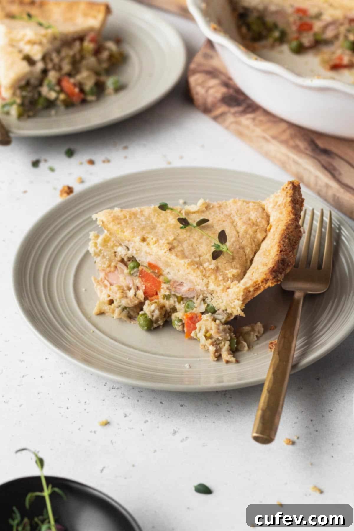 A generous slice of golden-brown vegan pot pie on a white plate, ready to be enjoyed with a elegant gold fork.