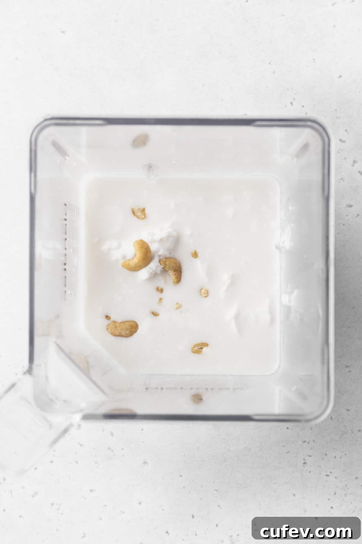 Coconut milk and thoroughly soaked raw cashews, ready to be blended into a creamy base for the pot pie filling, captured within a blender pitcher.
